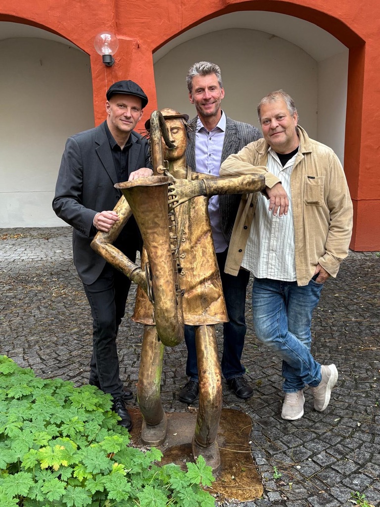 Three musicians posing with a saxophone sculpture